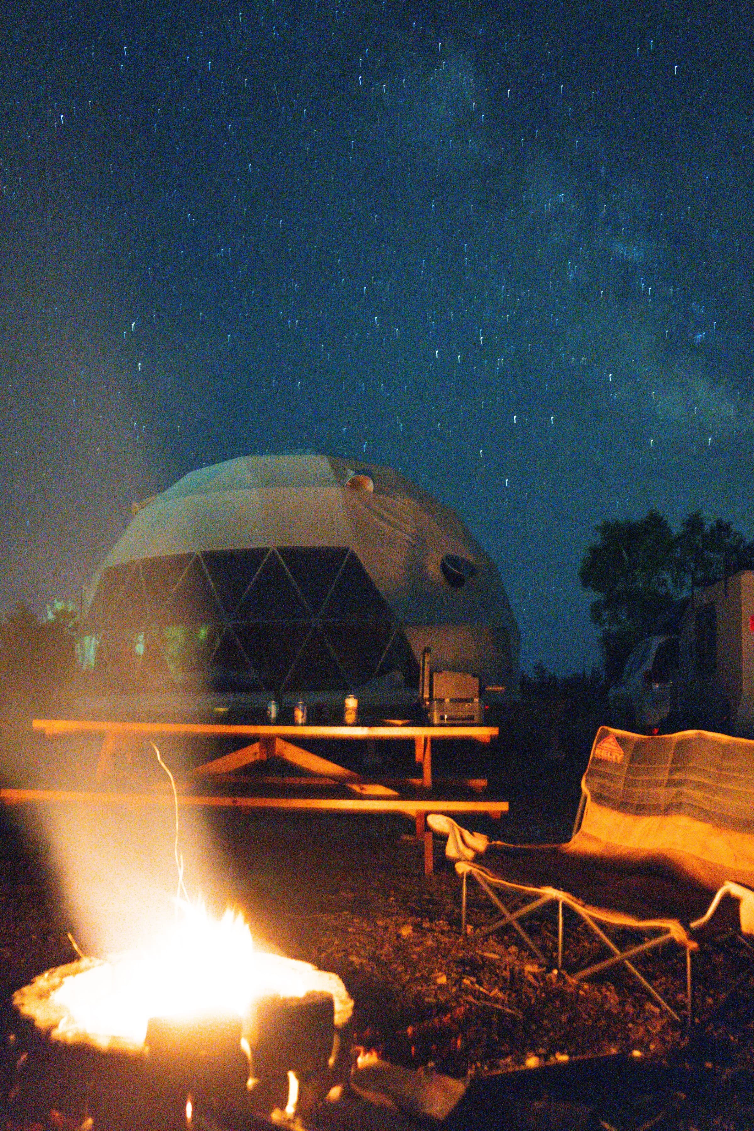 The Milky Way over a dome and campfire on a clear fall night