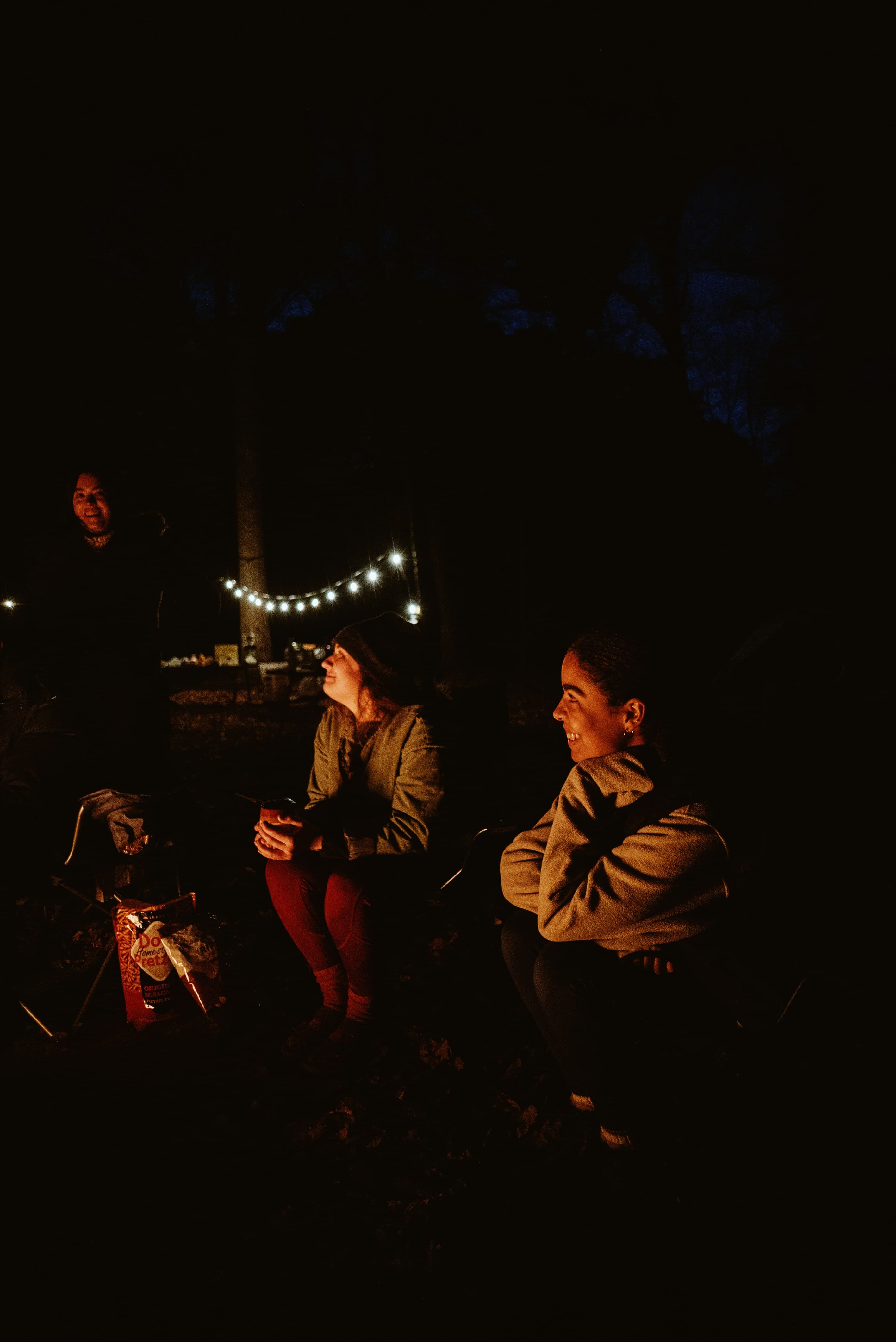 Friends around a campfire after dark under string lights