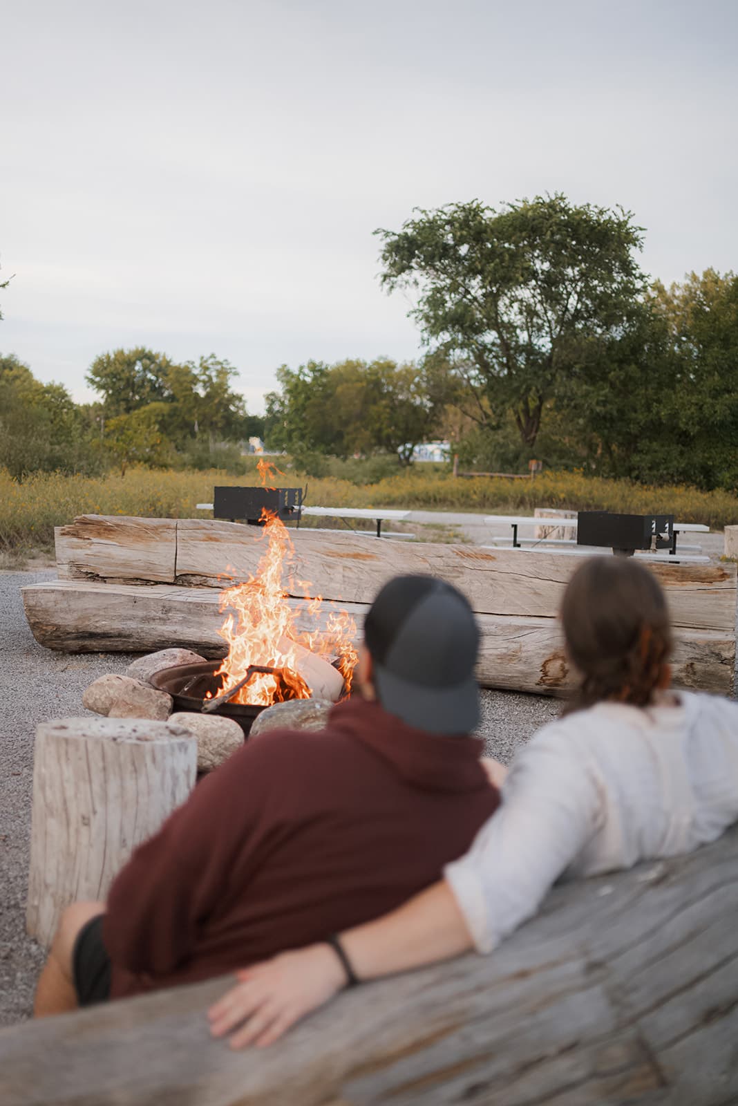 Two guests on a log bench beside the fire at the Commons